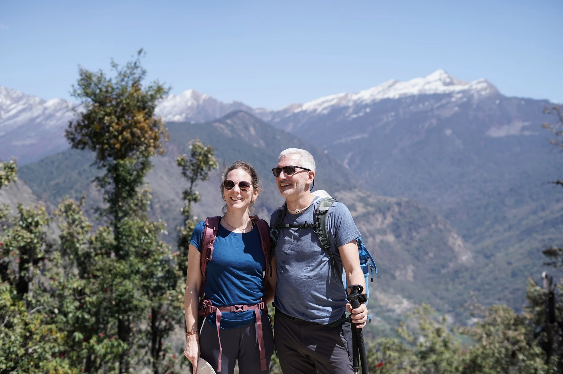 Two hikers together in front of the mountains, with one holding a trekking pole